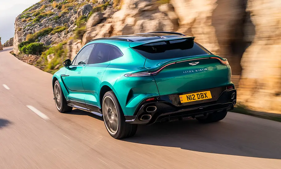 Der Aston Martin DBX S (2025) fahrend auf einer Straße von schräg hinten.