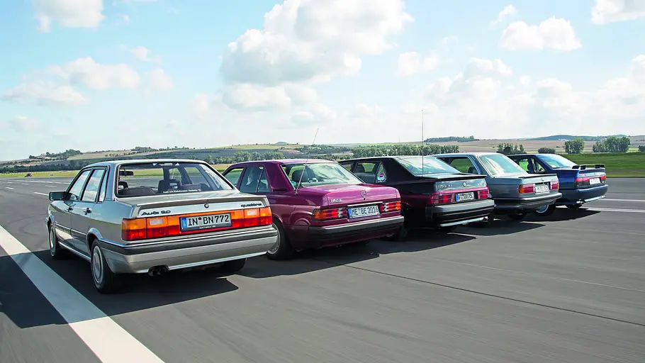 Audi 90 2.2 Quattro/Mercedes 190 E 2.6/Alfa Romeo 75 3.0 QV/BMW 325ix/Renault 21 Turbo Allrad fahrend von schräg hinten fotografiert. 
