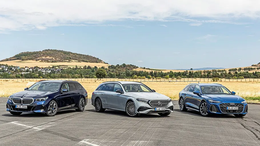 BMW 540d xDrive Touring, Mercedes E 450 d 4Matic T-Modell und Audi A6 Avant stehen nebeneinander vor hügeliger Landschaft