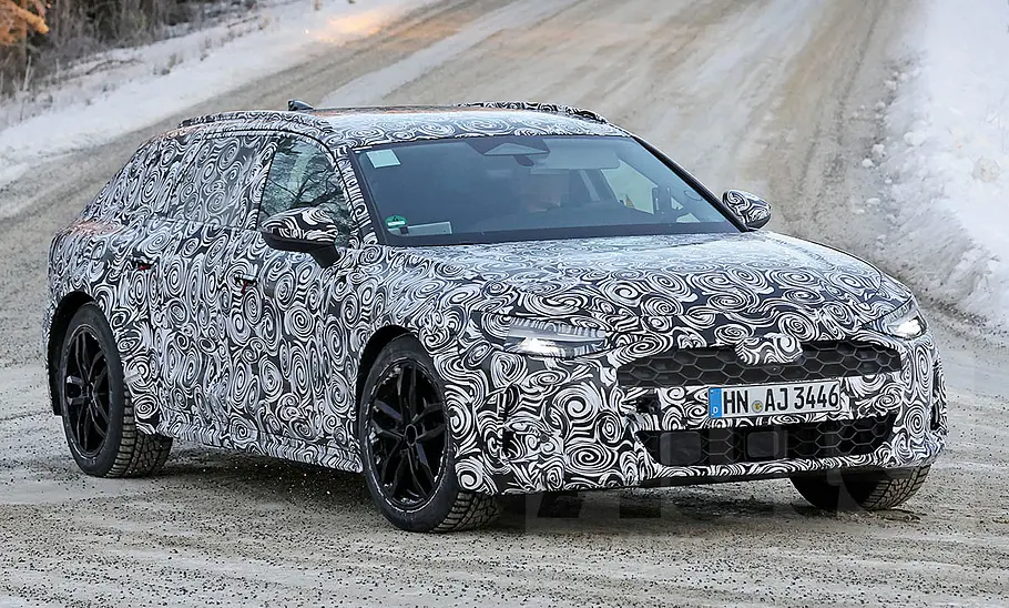 Der Audi A6 Allroad (2025) als Erlkönig fährt durch eine Kurve, von schräg vorne fotografiert.