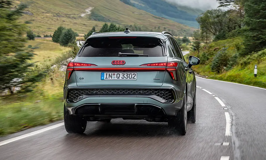 Der Audi Q3 (2025) fahrend auf einer Straße in der Ansicht von hinten, man sieht das beleuchtete Logo.