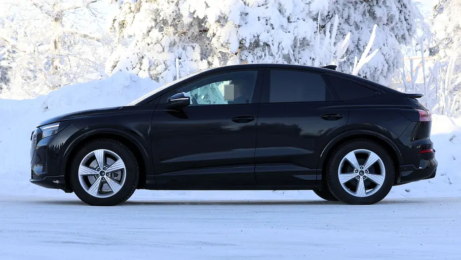 Der Audi Q4 Sportback e-tron fährt als Erlkönig auf einer verschneiten Straße, von links fotografiert.