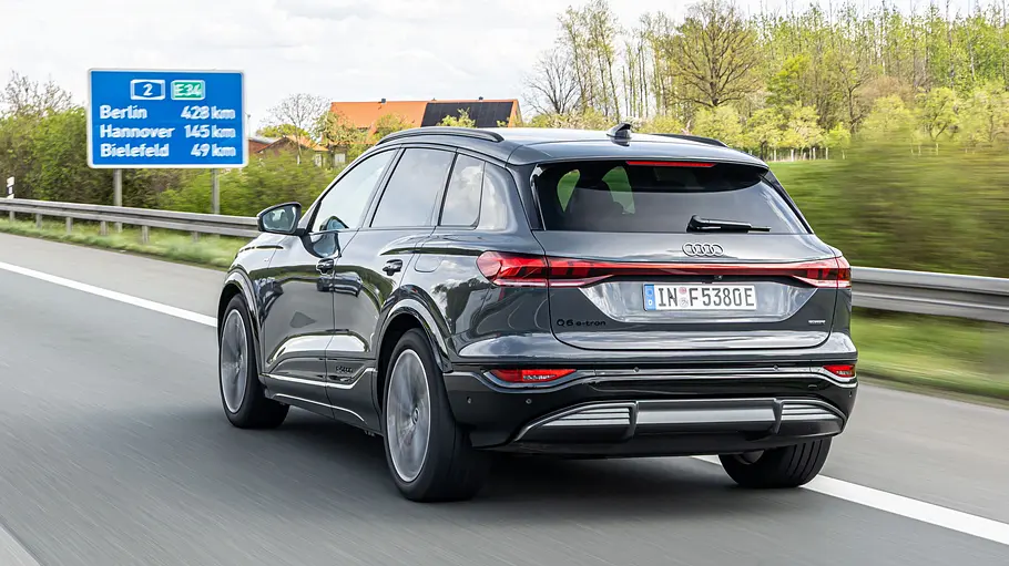 Ein grauer Audi Q6 e-tron fährt auf einer Autobahn, von schräg hinten gesehen. Am Straßenrand stehen ein blaues Schild und Bäume.