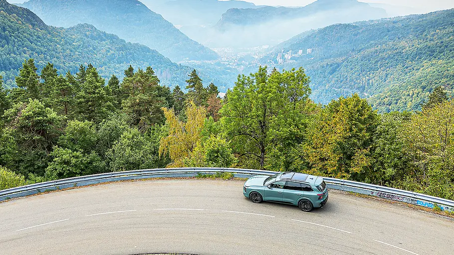 Audi Q7 (2026) Blick aus der Vogelperspektive auf den fahrenden Audi Q7 (2026) mit einer malerischen Hügellandschaft im Hintergrund.