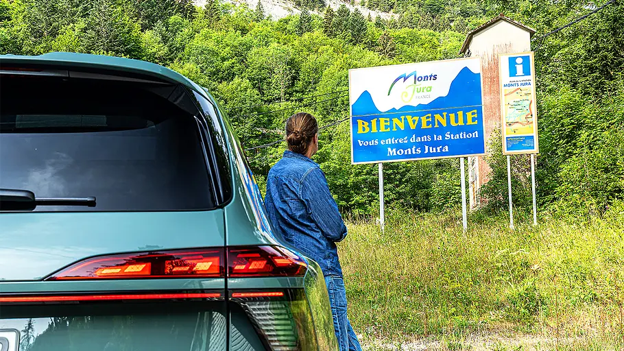 Audi Q7 (2026) Blick auf eine Person, die sich an den Audi Q7 (2026) anlehnt und ein Schild in der Ferne betrachtet.