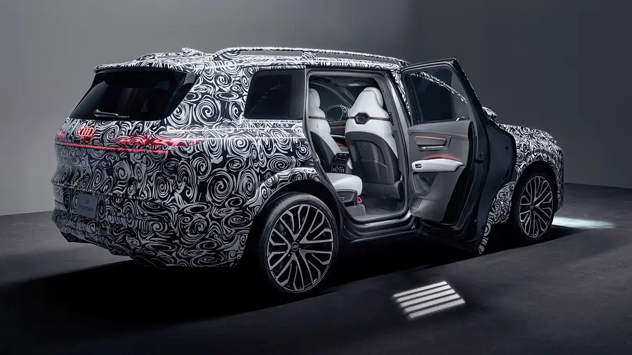 Audi Q9 (2026) Der Audi Q9 steht als Erlkönig mit geöffneter Hecktür in Studioumgebung, von hinten rechts fotografiert.