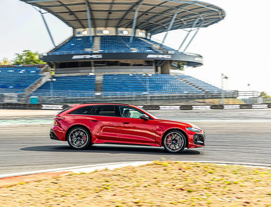 Audi RS 5 Avant im Tracktest Ein roter Audi RS 5 Avant fährt auf einer Rennstrecke an einer überdachten Tribüne mit leeren blauen Sitzreihen vorbei.
