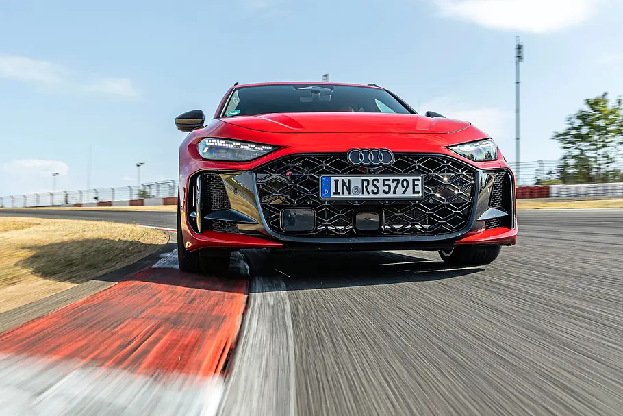Audi RS 5 Avant im Tracktest Ein roter Audi RS 5 Avant fährt auf einer Rennstrecke über rot-weiße Randsteine. Die Front ist aus niedriger Perspektive zu sehen.