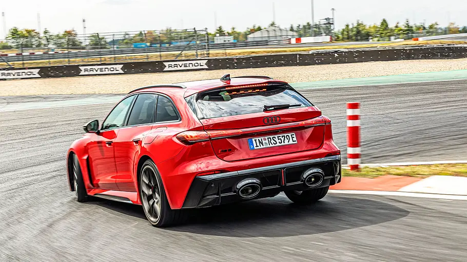 Audi RS 5 Avant Tracktest Ein roter Audi RS 5 Avant fährt durch eine Kurve auf einer Rennstrecke. Im Hintergrund sind Tribünen und blauer Himmel zu sehen.