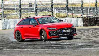 Ein roter Audi RS 5 Avant driftet durch eine Kurve auf einer Rennstrecke. Im Hintergrund sind Tribünen und blauer Himmel zu sehen. - Foto: Frank Ratering Ein roter Audi RS 5 Avant driftet durch eine Kurve auf einer Rennstrecke. Im Hintergrund sind Tribünen und blauer Himmel zu sehen. - Foto: Frank Ratering