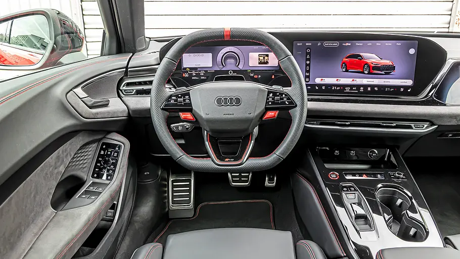 Audi RS 5 Avant Tracktest Das Audi RS 5 Cockpit zeigt ein Sportlenkrad, digitale Anzeigen und eine Mittelkonsole mit Getränkehaltern sowie rote Ziernähte.