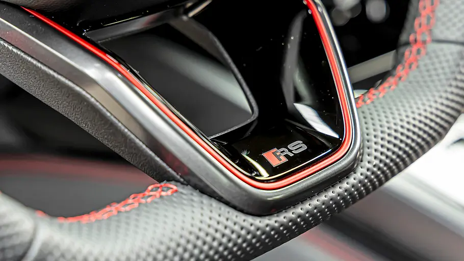 Audi RS 5 Avant Tracktest Das Lenkrad des Audi RS 5 Avant mit perforiertem schwarzem Leder, roten Nähten und einer glänzenden, rot umrandeten Speiche mit RS-Logo ist zu sehen.