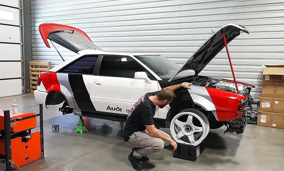 Audi Quattro S2 Coupé mit Bentley-W12 Blick von schräg vorne auf das Audi Quattro S2 Coupé mit Bentley-W12. Eine Person hockt neben dem rechten Vorderrad.
