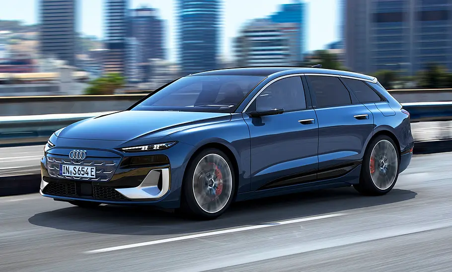 Der Audi S6 e-tron (2025) fährt vor urbanem Hintergrund über eine Straße, von vorne links fotografiert.