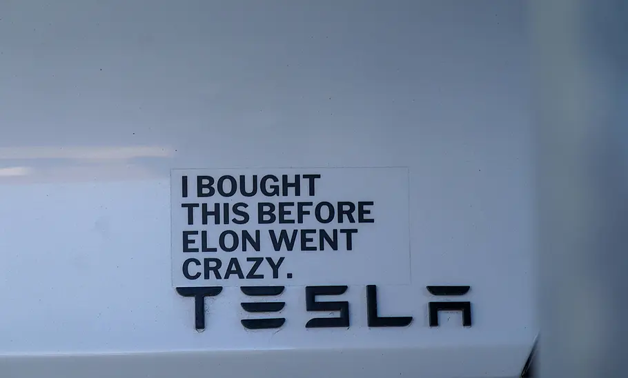 Ein Detailbild von einem Tesla, über dem Markenlogo sieht man den Sticker I bought this before Elon Musk went crazy.