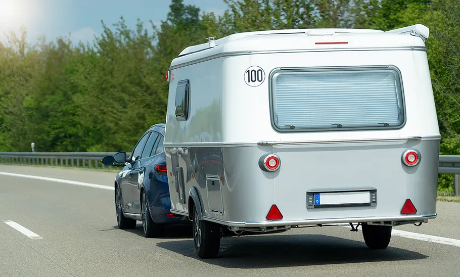 Ein Auto fährt über eine Straße und zieht einen kleinen Caravan.