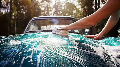 Die Motorhaube eines Auto wird mit einem Schwamm gewaschen. - Foto: iStock/stevecoleimages