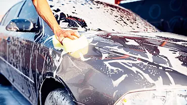 Auto zu Hause waschen: Symbolbild zeigt mit Schaum bedecktes Auto und eine Hand, die einen Schwamm auf dem Lack führt. - Foto: Imago