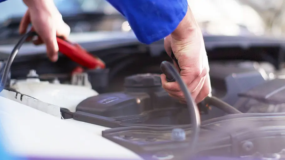 Autobatterie: Ladegerät kaufen Tester beim Anschließen eines Ladegeräts an eine Autobatterie, fotografiert von rechts.