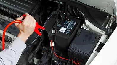 Ein Mechaniker klemmt ein Ladegerät an eine Autobatterie. - Foto: AZ Archiv