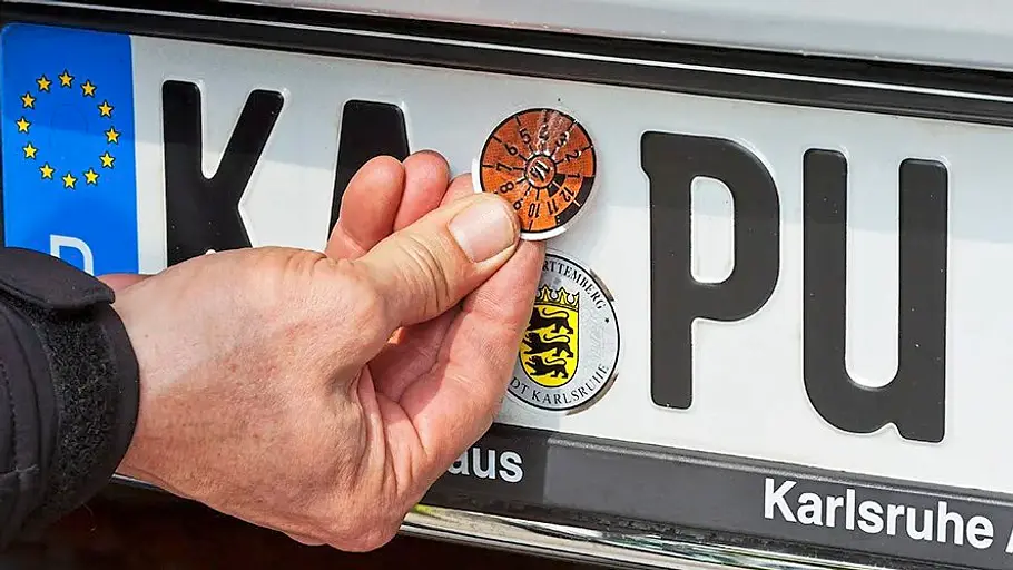 Wahrheit über Autokennzeichen Kennzeichen hinten mit Siegel der Zulassungsstelle und der aktuellen HU-Prüfplakette.
