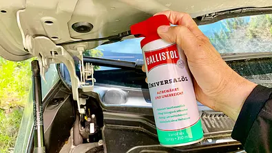Hand mit Ballistol-Spraydose über Motorraum eines Autos. - Foto: Holger Ippen