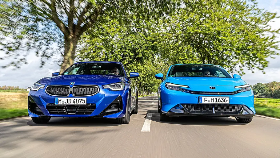 BMW 2er Coupé gegen Honda Prelude im Vergleichstest Ein dunkelblaues BMW 2er Coupé und ein hellblauer Honda Prelude fahren nebeneinander auf einer baumgesäumten Straße, von vorn gesehen.