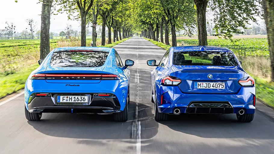 BMW 2er Coupé gegen Honda Prelude im Vergleichstest Ein hellblauer Honda Prelude und ein blauer BMW 220i fahren nebeneinander auf einer Allee, von hinten gesehen.