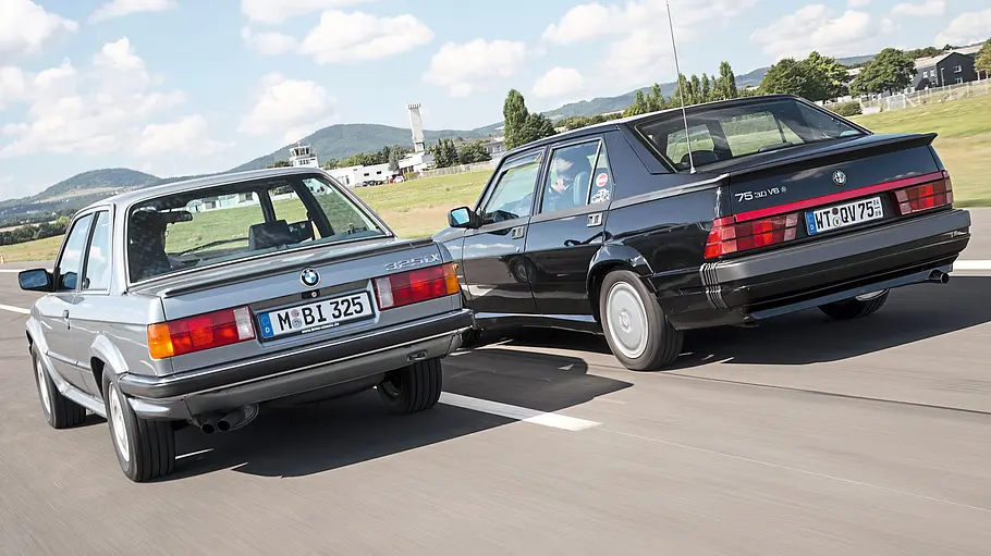 BMW 325ix/Alfa Romeo 75 3.0 QV fahrend von schräg hinten fotografiert. 
