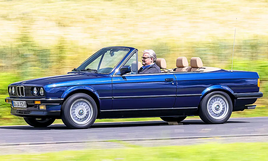 Der fahrende BMW 3er in der Seitenansicht. Das Verdeck ist geöffnet, man sieht einen Mann am Steuer.
