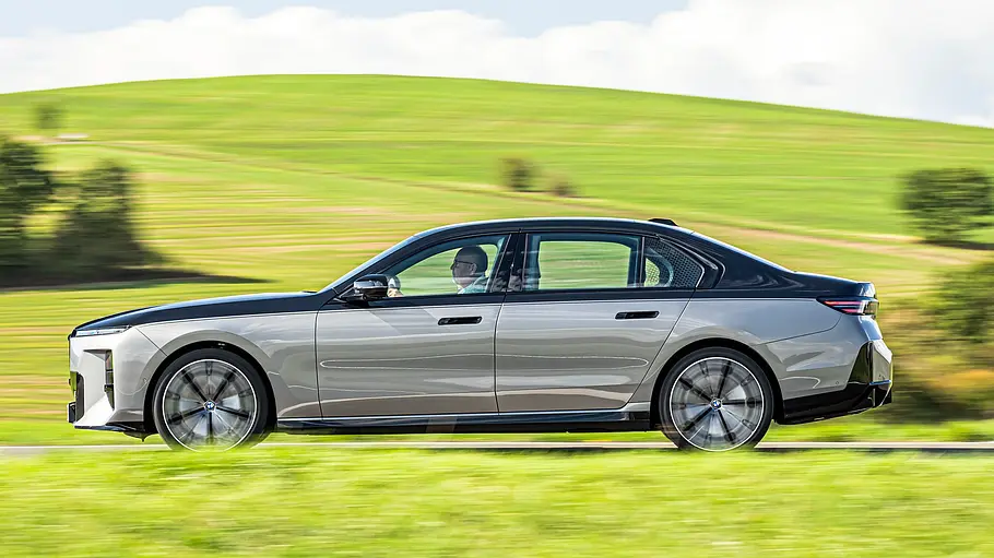 BMW 740 xDrive Einzeltest 7er Facelift Ein BMW 7er mit schwarzem Dach fährt auf einer Straße vor grünen Hügeln unter bewölktem Himmel.