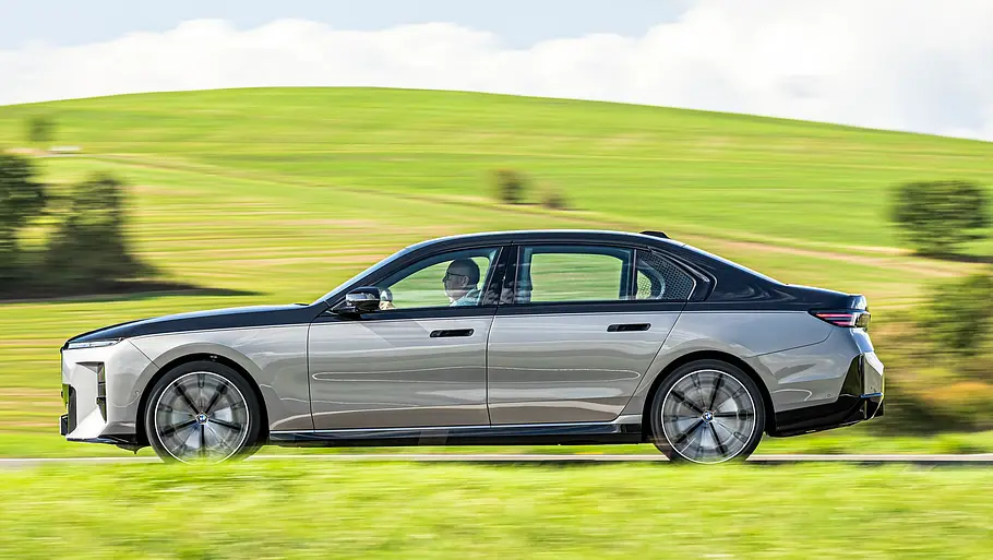 BMW 740 xDrive Einzeltest 7er Facelift Eine silber-schwarze BMW 7er Facelift Limousine mit Zweifarb-Lackierung fährt auf einer Landstraße, umgeben von grünen Wiesen unter blauem Himmel.