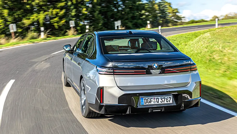 BMW 740 xDrive Einzeltest 7er Facelift Eine silber-schwarze BMW 7er Facelift Limousine mit Zweifarb-Lackierung fährt auf einer Landstraße, umgeben von grünen Wiesen unter blauem Himmel.