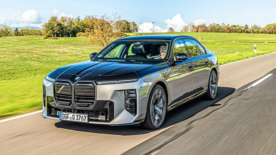 BMW 740 xDrive Einzeltest 7er Facelift Eine silber-schwarze BMW 7er Facelift Limousine mit Zweifarb-Lackierung fährt auf einer Landstraße, umgeben von grünen Wiesen unter blauem Himmel.
