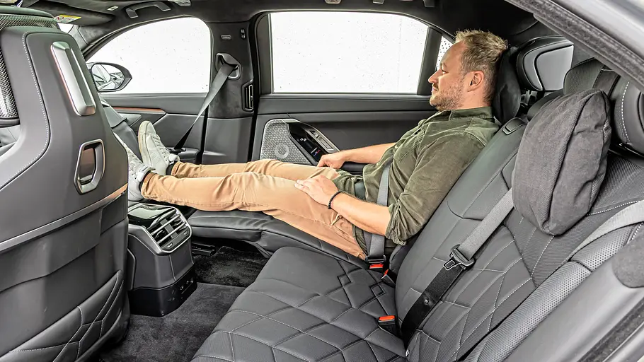 BMW 740 xDrive Einzeltest 7er Facelift Ein angeschnallter Mann sitzt mit ausgestreckten Beinen auf einem zurückgelehnten Rücksitz im schwarzen Lederinterieur des BMW 7er.