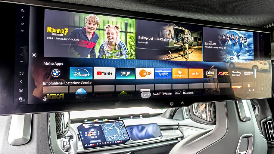 BMW 740 xDrive Einzeltest 7er Facelift Ein großer Breitbildschirm mit Streaming-Apps hängt im Innenraum des BMW 7er vor den Rücksitzen. Darunter ist das Cockpit sichtbar.