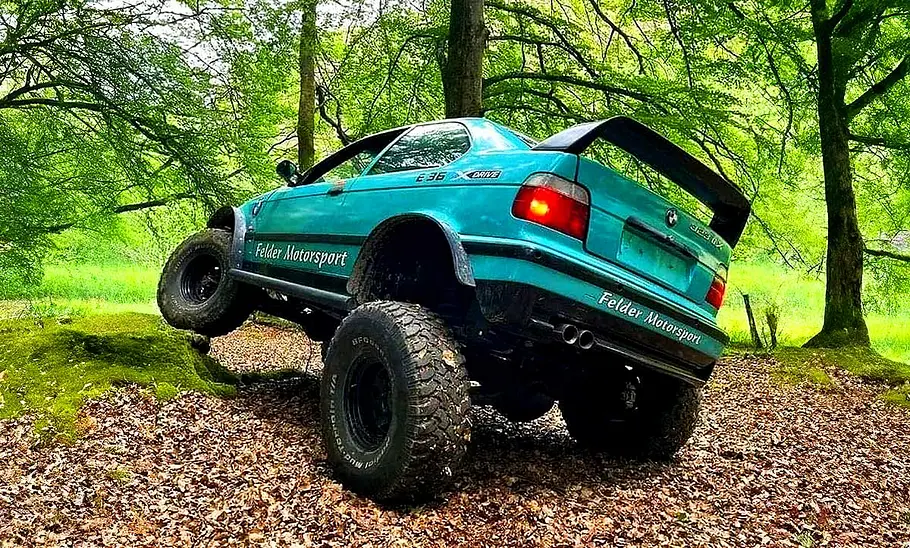Blick von schräg hinten auf den BMW 3er E36 Offroader, der ein Hindernis überwindet.