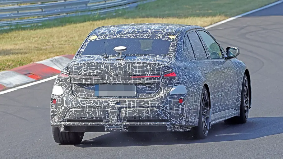 BMW i3 M (2027) Der BMW i3 M fährt als Erlkönig auf einer Rennstrecke, von hinten fotografiert.