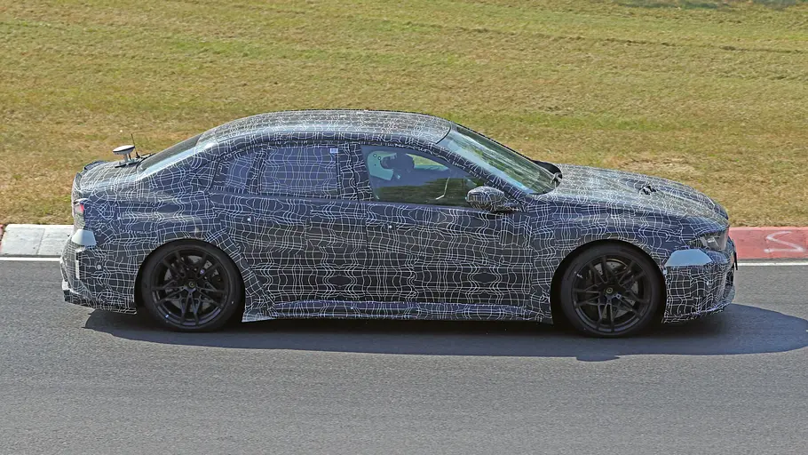 BMW i3 M (2027) Der BMW i3 M fährt als Erlkönig auf einer Rennstrecke, von rechts fotografiert.