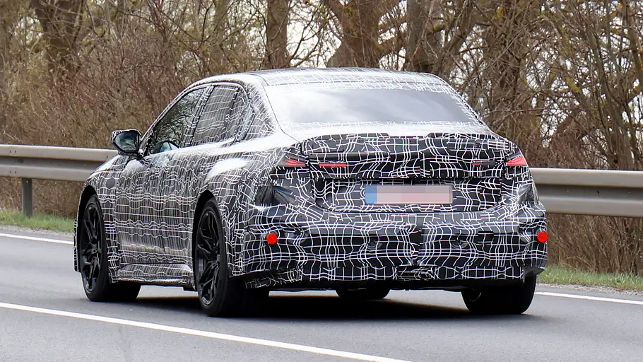 Der BMW i3 M fährt als Erlkönig auf einer Landstraße, von vorne links fotografiert.