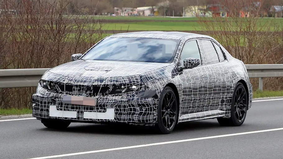 Der BMW i3 M fährt als Erlkönig auf einer Landstraße, von vorne links fotografiert.