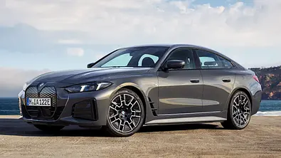 Der BMW i4 statisch von schräg vorne links vor einem Küstenabschnitt fotografiert. - Foto: BMW