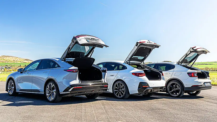 Blick von schräg hinten auf die drei Elektro-Limousinen Mazda 6e, BMWi4 und Polestar 2 mit geöffnetem Kofferraum.