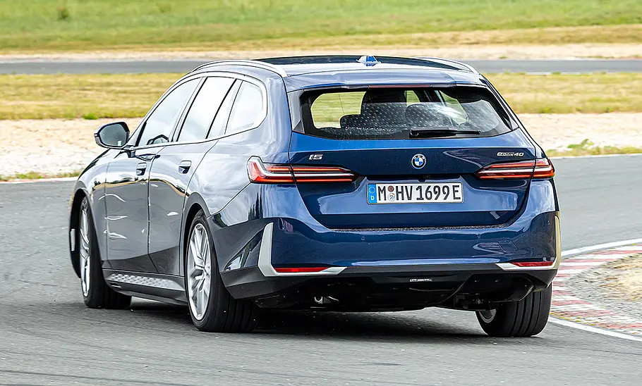 Der BMW i5 Touring fährt durch eine Kurve, von hinten fotografiert.