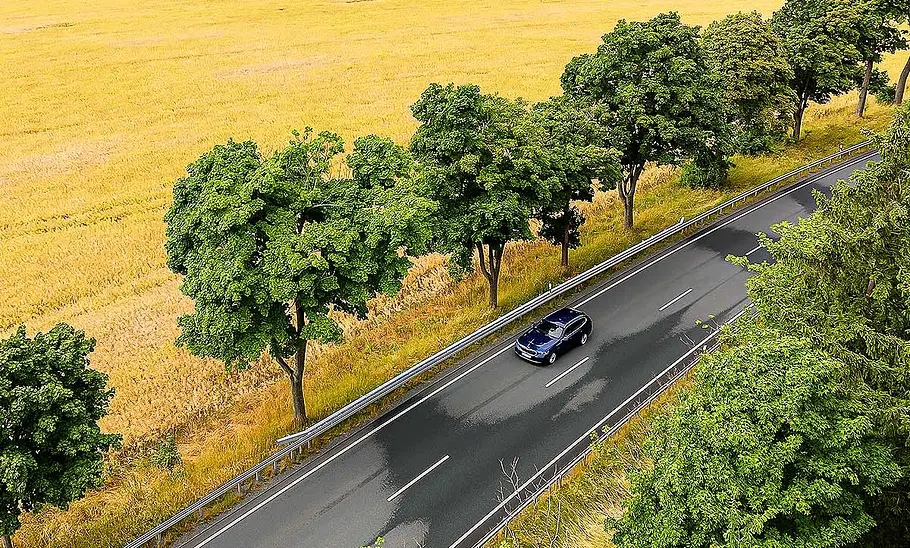 BMW i5 Touring Blick von schräg vorne aus der Vogelperspektive auf den BMW i5 Touring, der über eine von Bäumen umgebene Landstraße fährt.