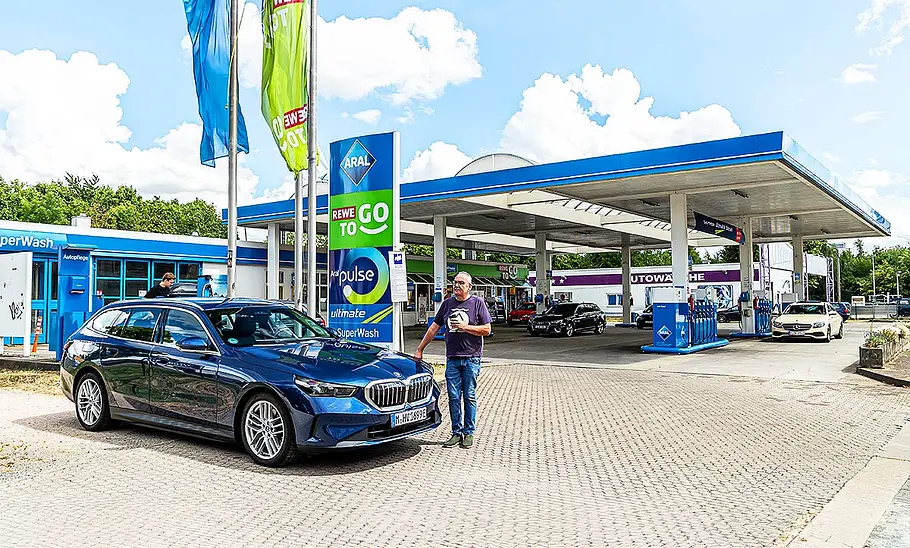 BMW i5 Touring Blick von schräg vorne auf den BMW i5 Touring, der an einer Aral-Tankstelle Halt macht.