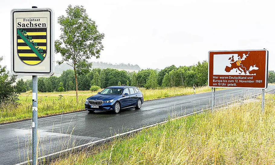 BMW i5 Touring Blick von schräg vorne auf den BMW i5 Touring, der auf einer Landstraße entlang fährt.