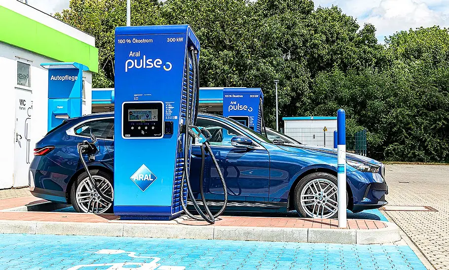 BMW i5 Touring Blick von der Seite auf den BMW i5 Touring, der an einer Schnellladesäule angeschlossen ist.