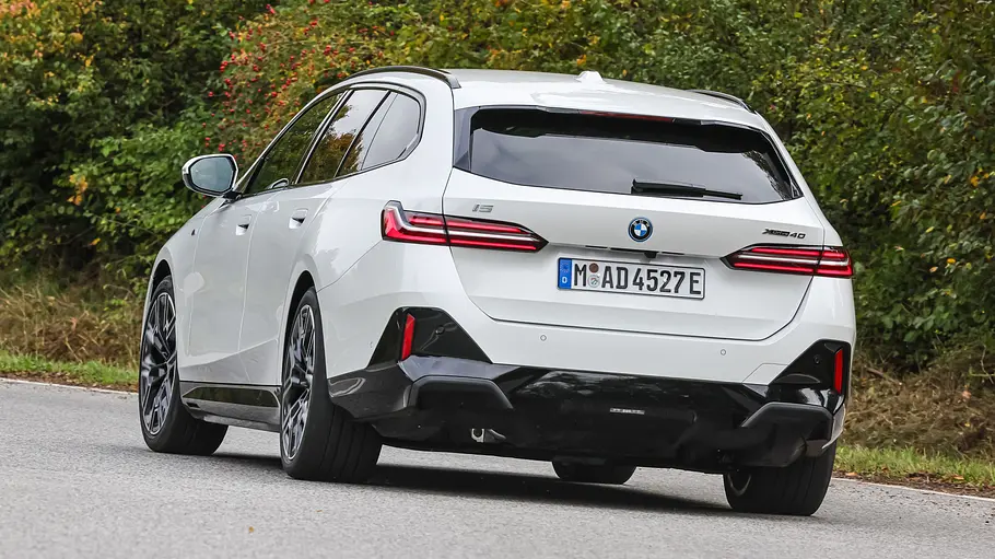 BMW i5 Touring Der BMW i5 Touring fährt durch eine Linkskurve, von hinten fotografiert.