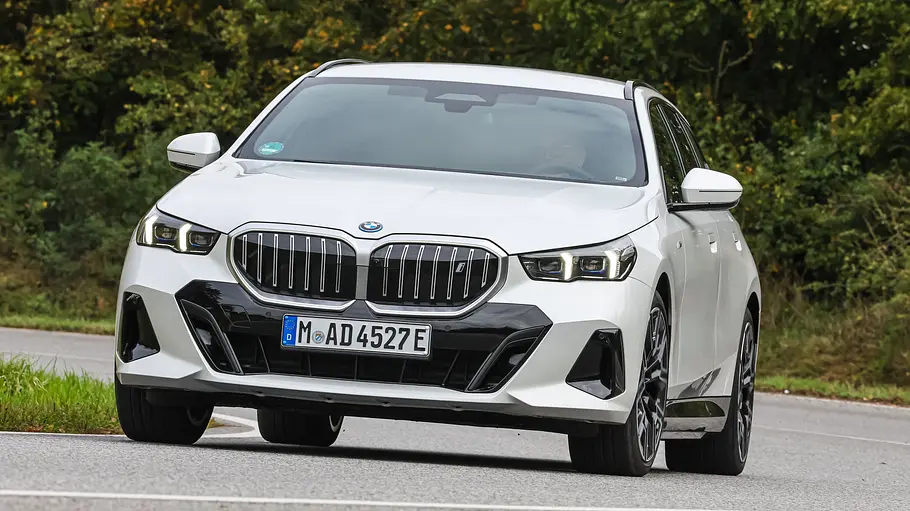 BMW i5 Touring Der BMW i5 Touring fährt durch eine Rechtskurve, von vorne fotogtafiert.
